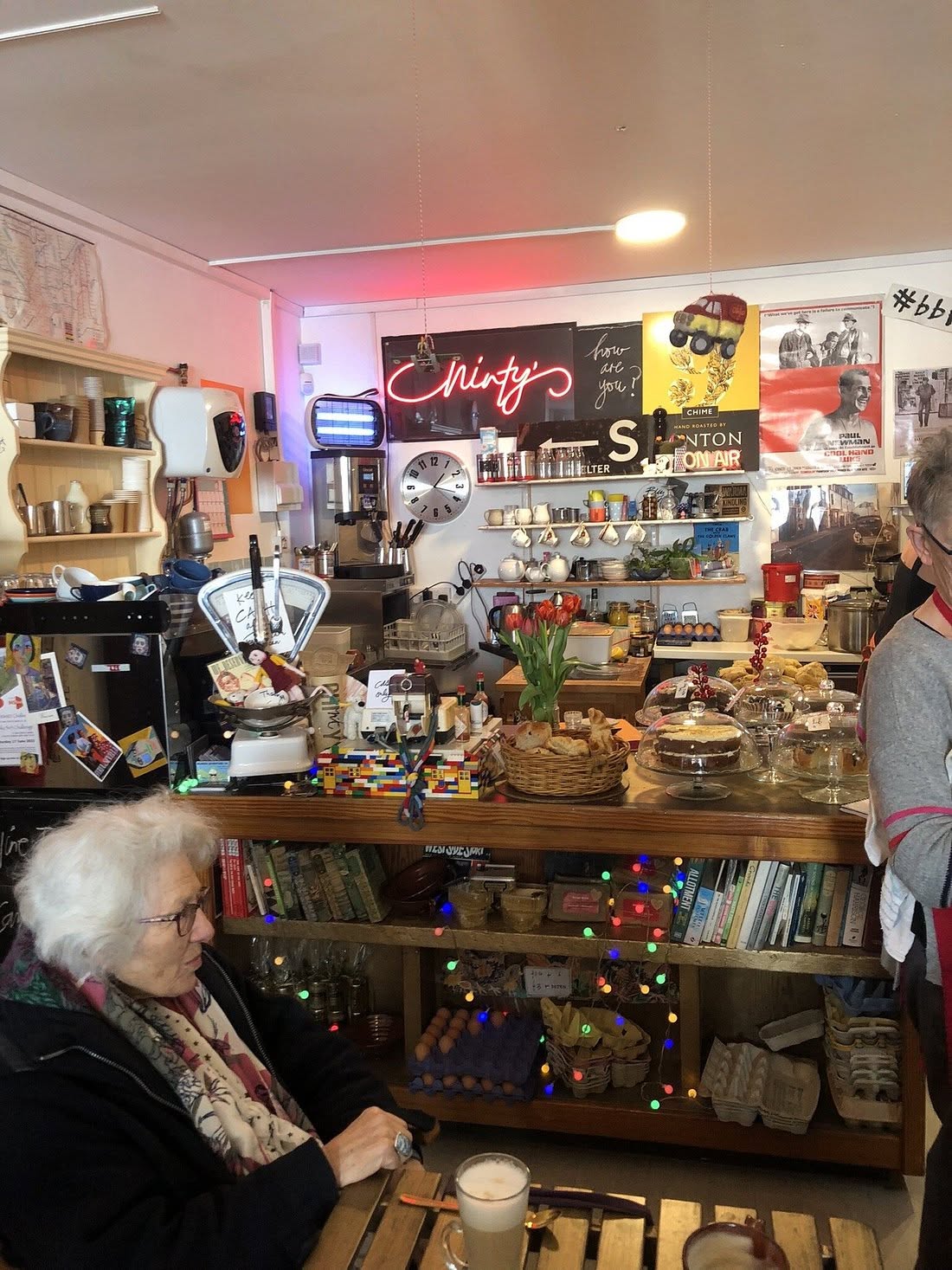 Inside Chinty's, with the red neon name sign, cake counter, pottery, books, postcards and visitors