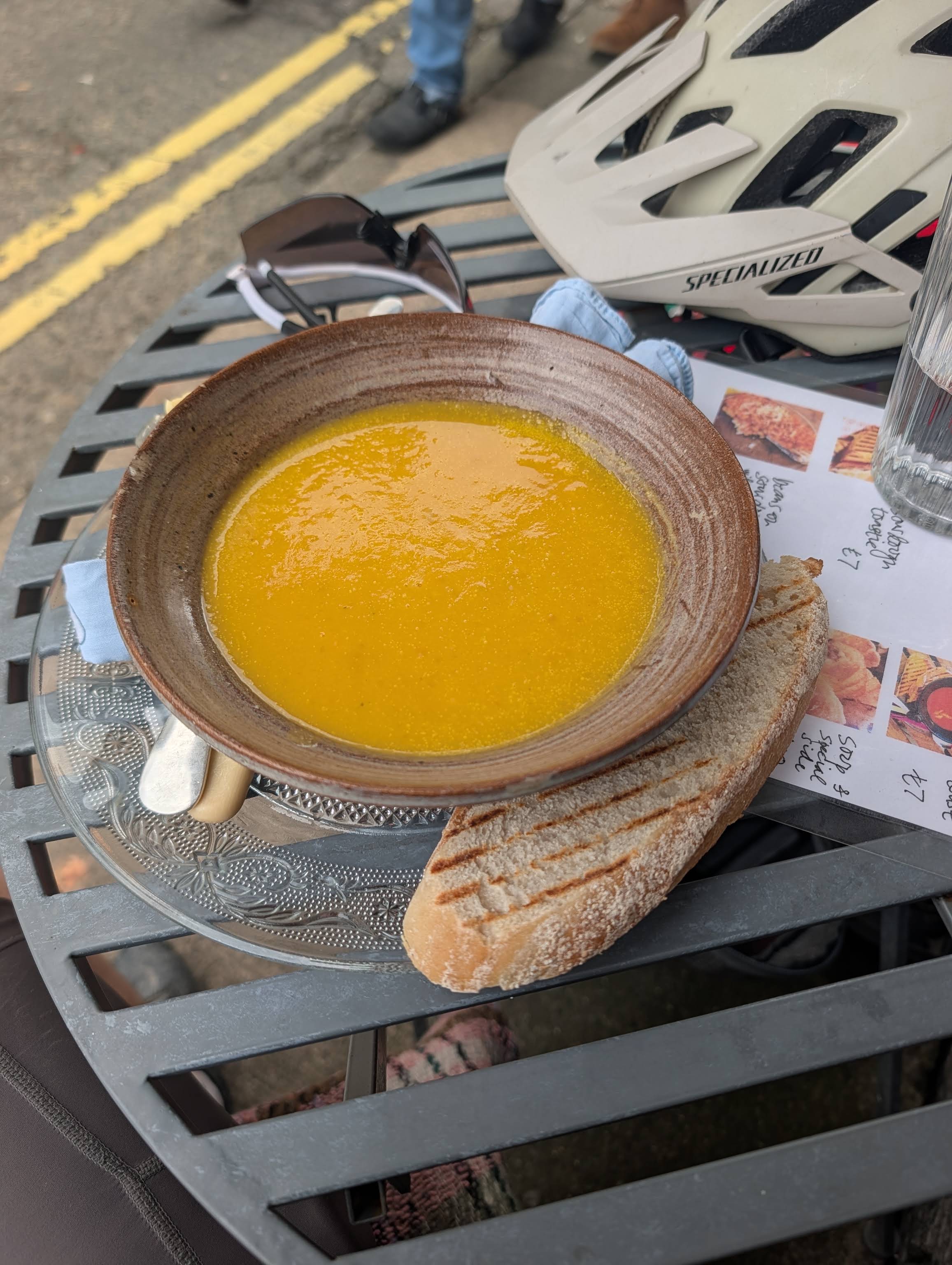 A complete pottery bowl of yellow soup and grilled bread on a patterned glass plate outside Chinty's